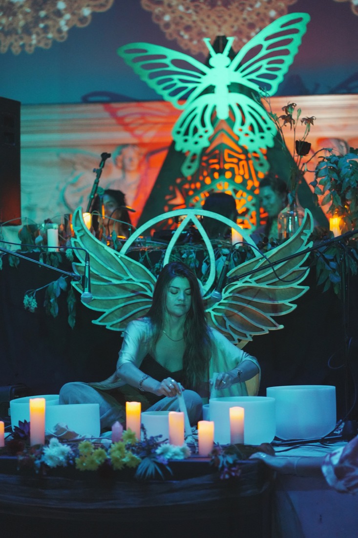 Crystal bowls and candles beneath glowing owl wings in a BAE temple